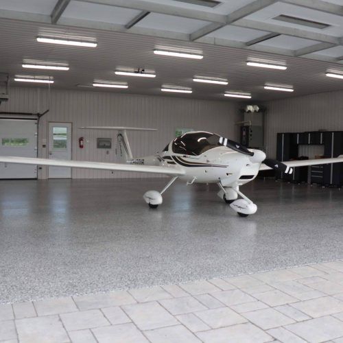 alt="big garage for little plane, floor made of polyaspartic with vinyl flakes that can resist to high traffic such as a plane"